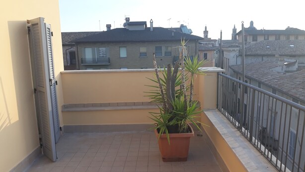 A balcony with a potted plant, a sliding door, and a view of buildings in the background. - Hotel La Torretta (Foligno)