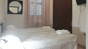 A bedroom with a bed, a window with blinds, a mirror, a wardrobe, and a TV mounted on the wall. - Hotel La Torretta (Foligno)