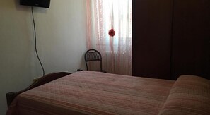 A bedroom with a bed, a chair, a TV mounted on the wall, and a window with curtains. - Hotel La Torretta (Foligno)