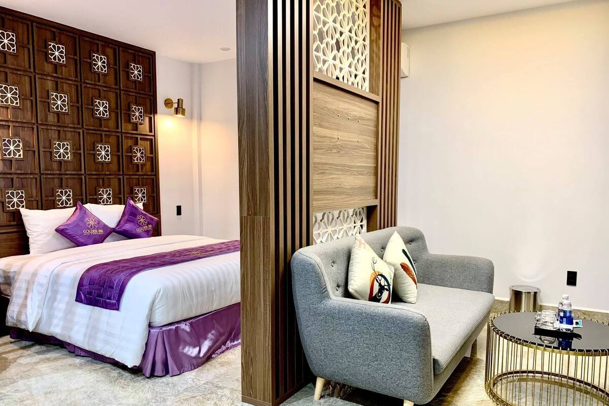 A hotel room with a bed, a grey sofa, a round coffee table, and a decorative wall panel.