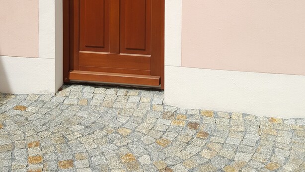 A wooden door with a glass panel, set in a building with a pink exterior and a cobblestone ground. - Vacation apartment in a farmhouse in beautiful Maxen in Müglitztal, near Dresden. (Müglitztal)