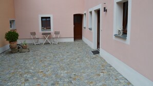 A courtyard with a stone floor, two chairs, a table, and a potted plant. - Vacation apartment in a farmhouse in beautiful Maxen in Müglitztal, near Dresden. (Müglitztal)