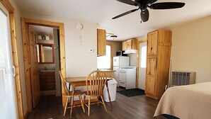 Ein kleines Zimmer mit Esstisch, Stühlen, Deckenventilator und einem Bett.