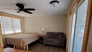 Ein gemütlicher Raum mit Bett, einer Schlafcouch, einem Esstisch mit Stühlen, einem Deckenventilator und einem großen Fenster.