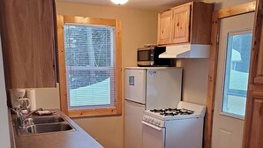 Eine kompakte Küche mit Holzausstattung, einer Mikrowelle, einem Kühlschrank, einem Herd und einem Spülbecken.