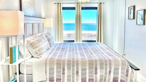 A bedroom with a bed, a ceiling fan, a nightstand, and a view of the ocean. - Island Winds East 202 – Beachfront Condo Steps from The Hangout & Attractions (Gulf Shores)