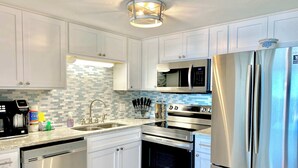 A modern kitchen with white cabinets, stainless steel appliances, a microwave, oven, and dishwasher. - Island Winds East 202 – Beachfront Condo Steps from The Hangout & Attractions (Gulf Shores)