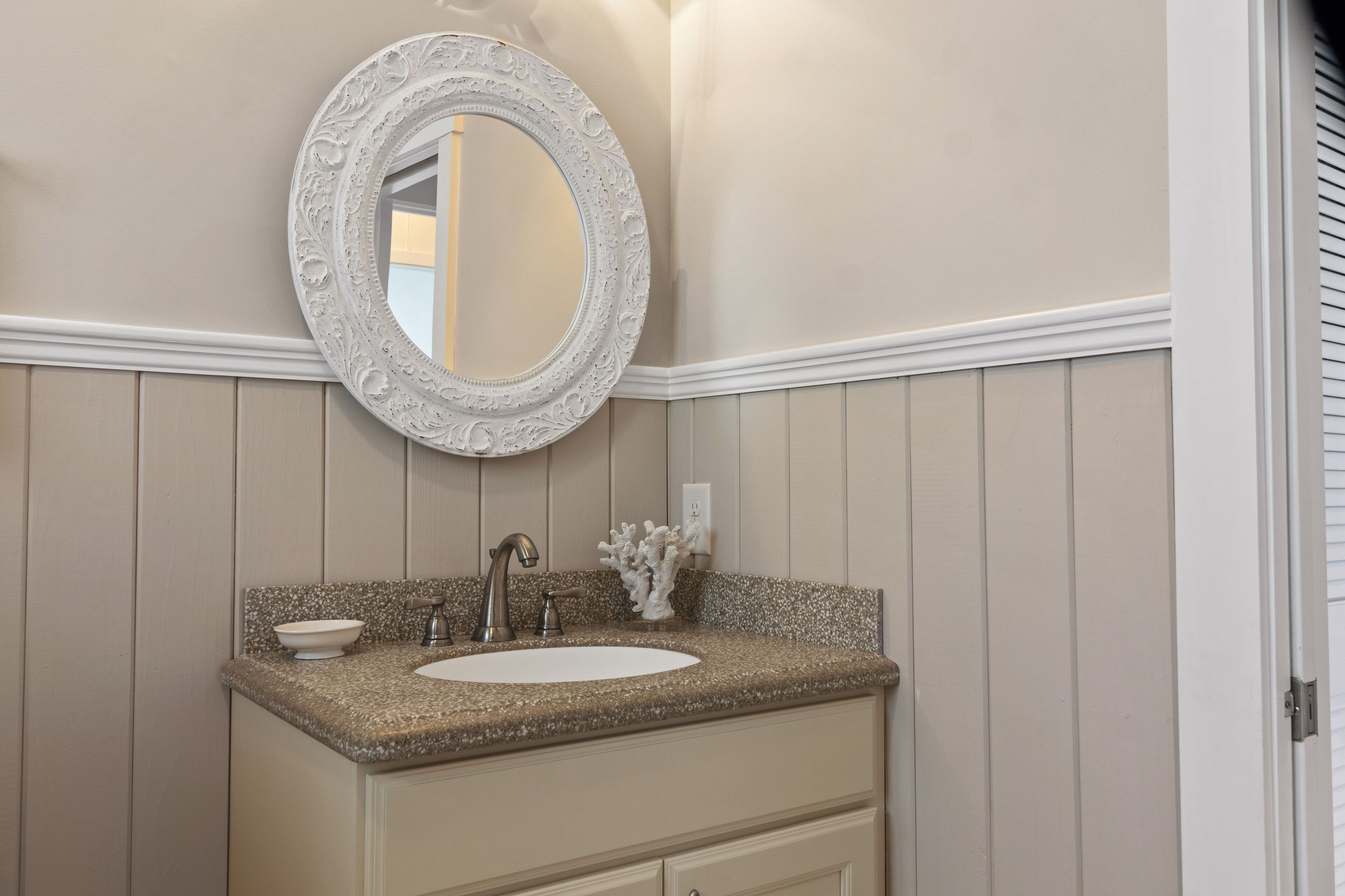 Un bagno con un piano in granito, un lavandino bianco, uno specchio decorativo e un interruttore della luce a parete.