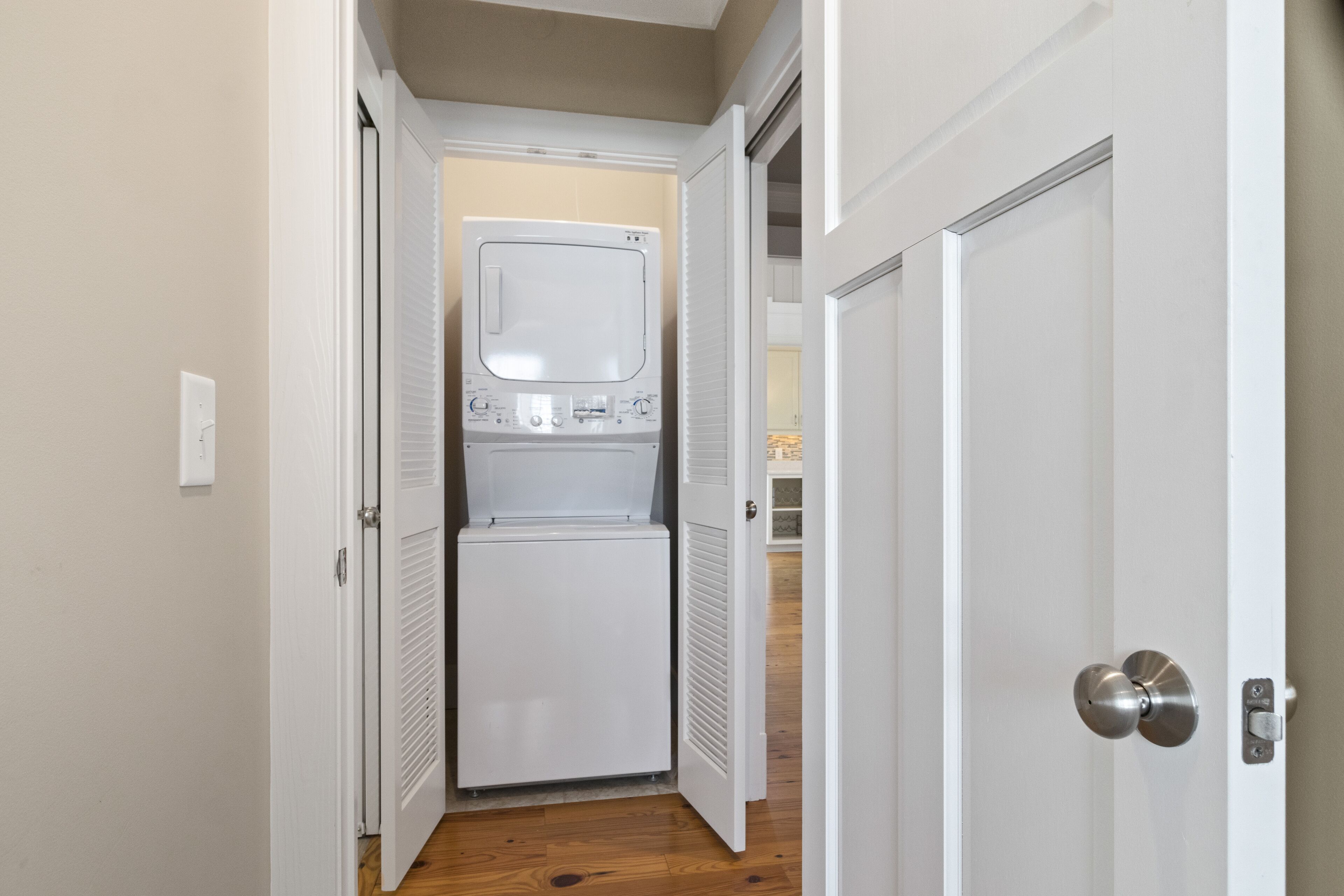 A laundry room with a washer and dryer, a door with a silver handle, and a wooden floor.