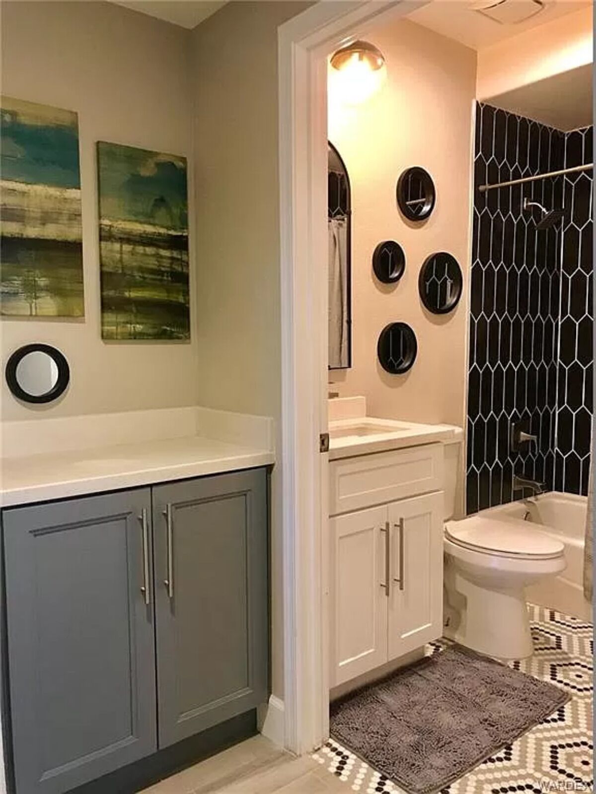 A bathroom with a grey cabinet, a white sink, a mirror, and a black and white patterned shower enclosure.