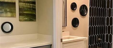 A bathroom with a grey cabinet, a white sink, a mirror, and a black and white patterned shower enclosure.