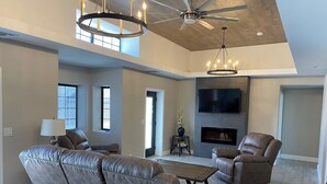A spacious living room with a leather sofa, a recliner, a coffee table, a fireplace, and a flat-screen TV mounted on the wall. - Bullhead oasis! Enjoy putt putt, view, pool & heated spa! (Bullhead City)