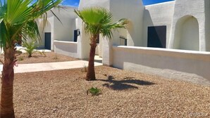 A modern building with white walls and arched windows, surrounded by gravel and palm trees. - Bullhead oasis! Enjoy putt putt, view, pool & heated spa! (Bullhead City)