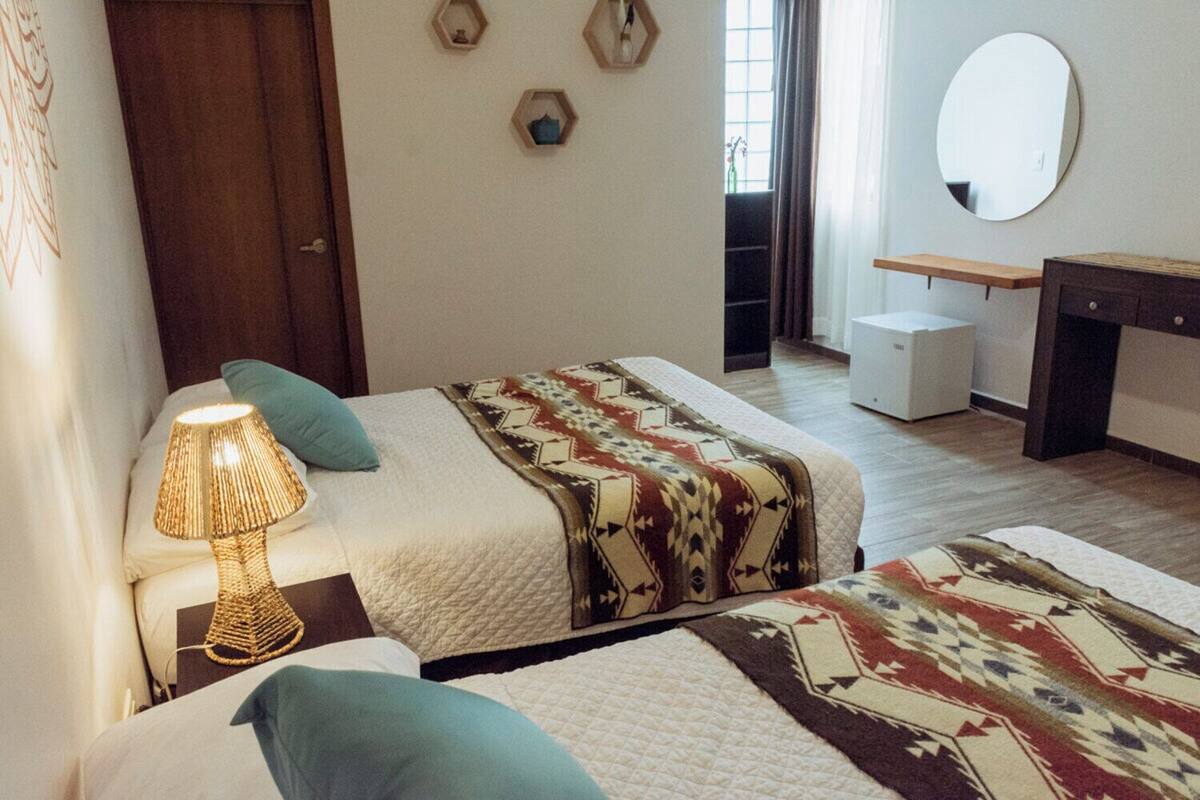 A bedroom with two beds, a bedside lamp, a desk, a mirror, and a window.