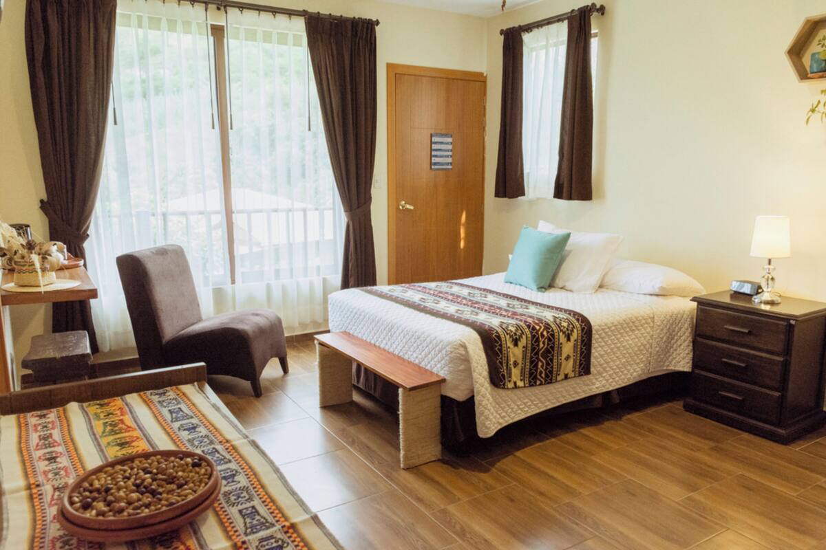 A bedroom with a bed, a bench, a chair, a bedside table, and a nightstand.