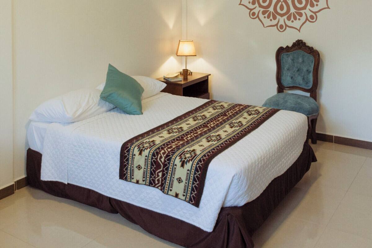 A bedroom with a bed, a nightstand, a chair, a wall decoration, and a ceiling light.
