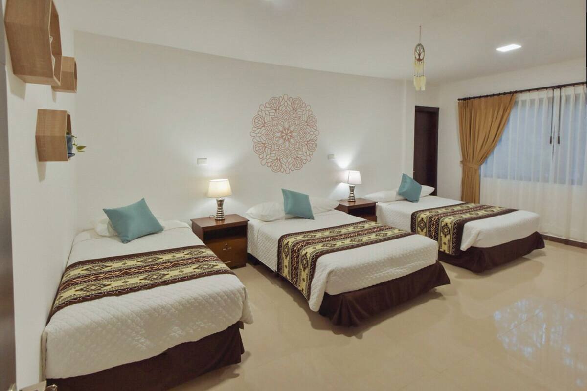 A hotel room with three beds, each with a patterned bedspread, bedside lamps, and a decorative wall piece.