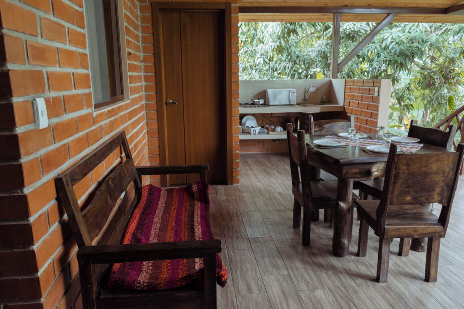 Une pièce avec un mur en briques, une porte en bois, un banc, une table avec des chaises et une petite kitchenette équipée d’un four à micro-ondes.