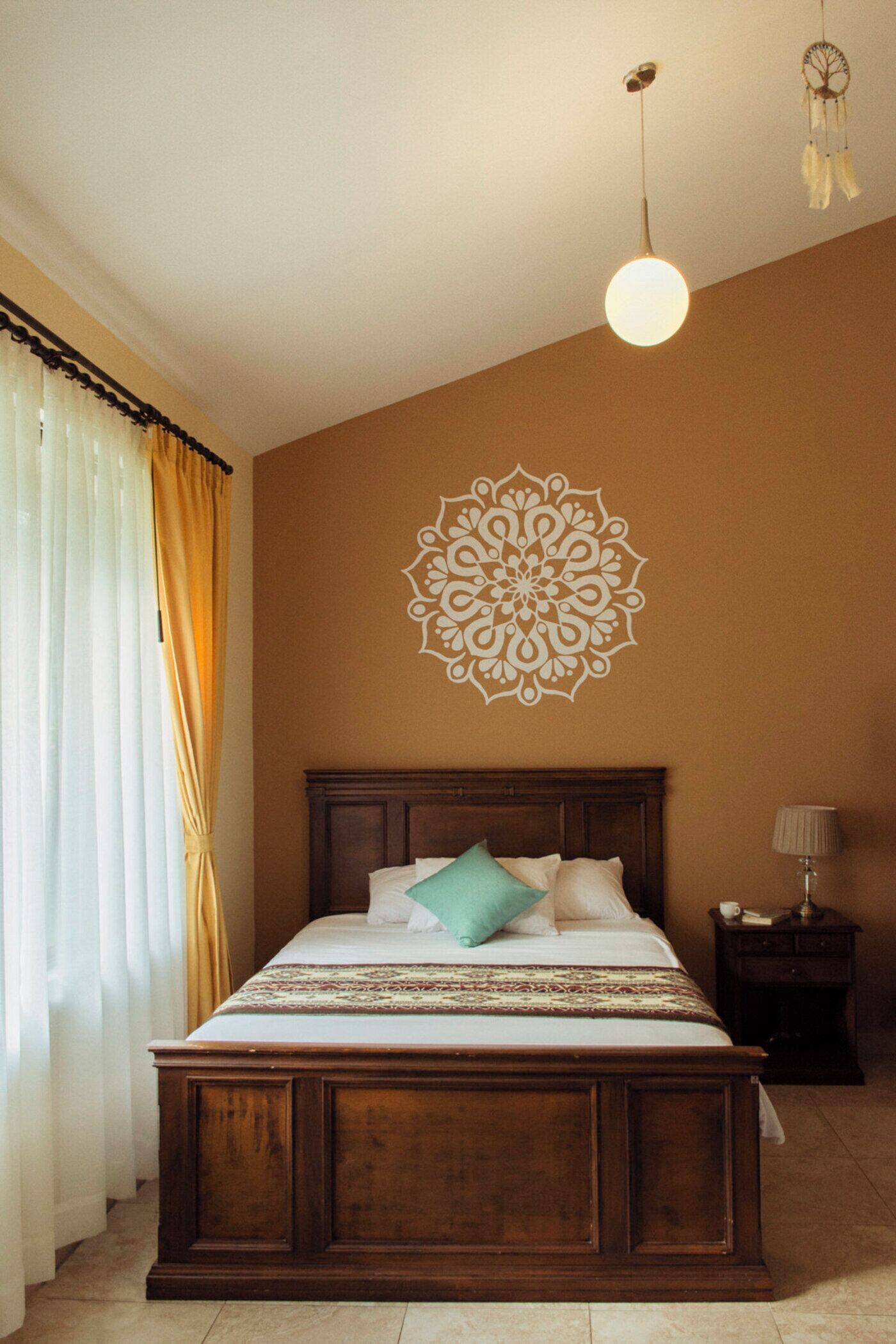 A bedroom with a wooden bed, a decorative wall piece, a bedside lamp, and a window with curtains.