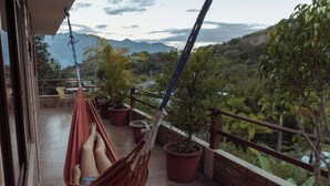 Un balcon avec un hamac, des plantes en pot et une vue sur les montagnes.