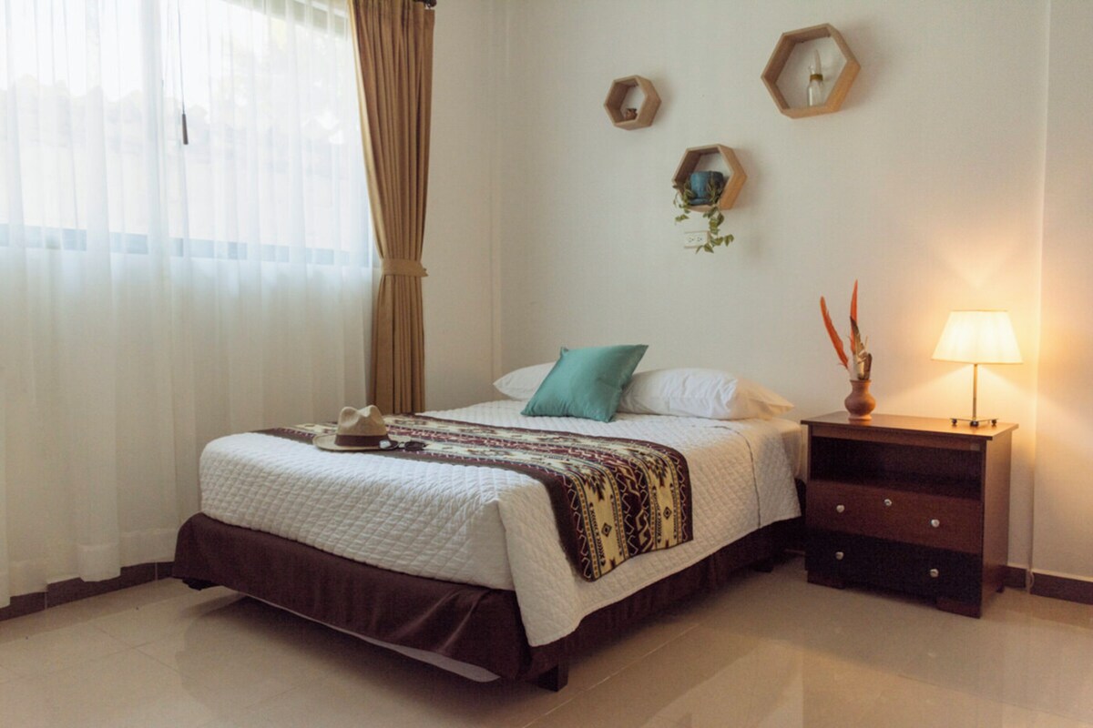 A neatly made bed with a patterned bedspread, a bedside table with a lamp, and wall-mounted decor.