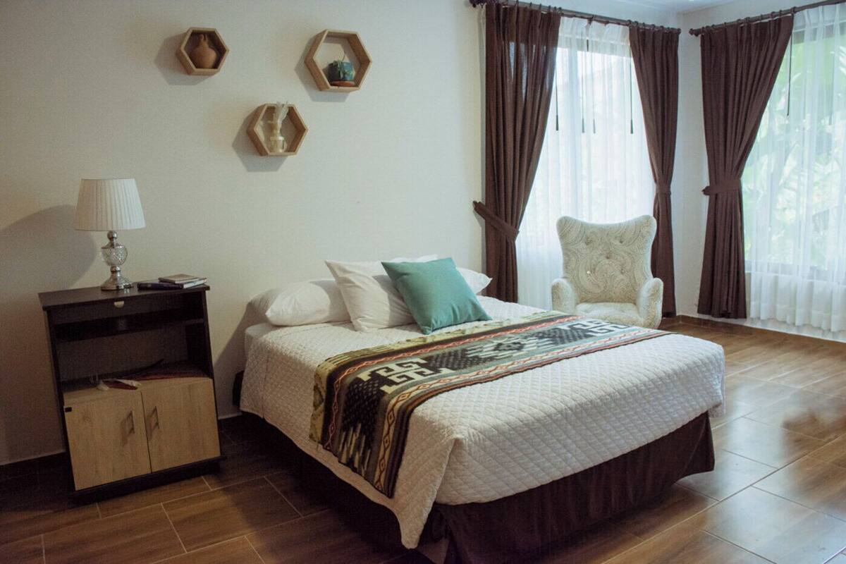 A neatly arranged bedroom with a bed, a chair, a nightstand, and decorative wall pieces.