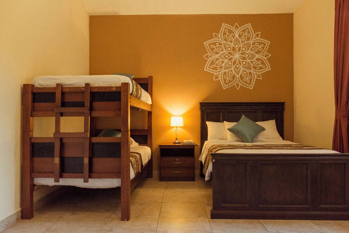 A room with a bunk bed, a single bed, a nightstand with a lamp, and a decorative wall piece.