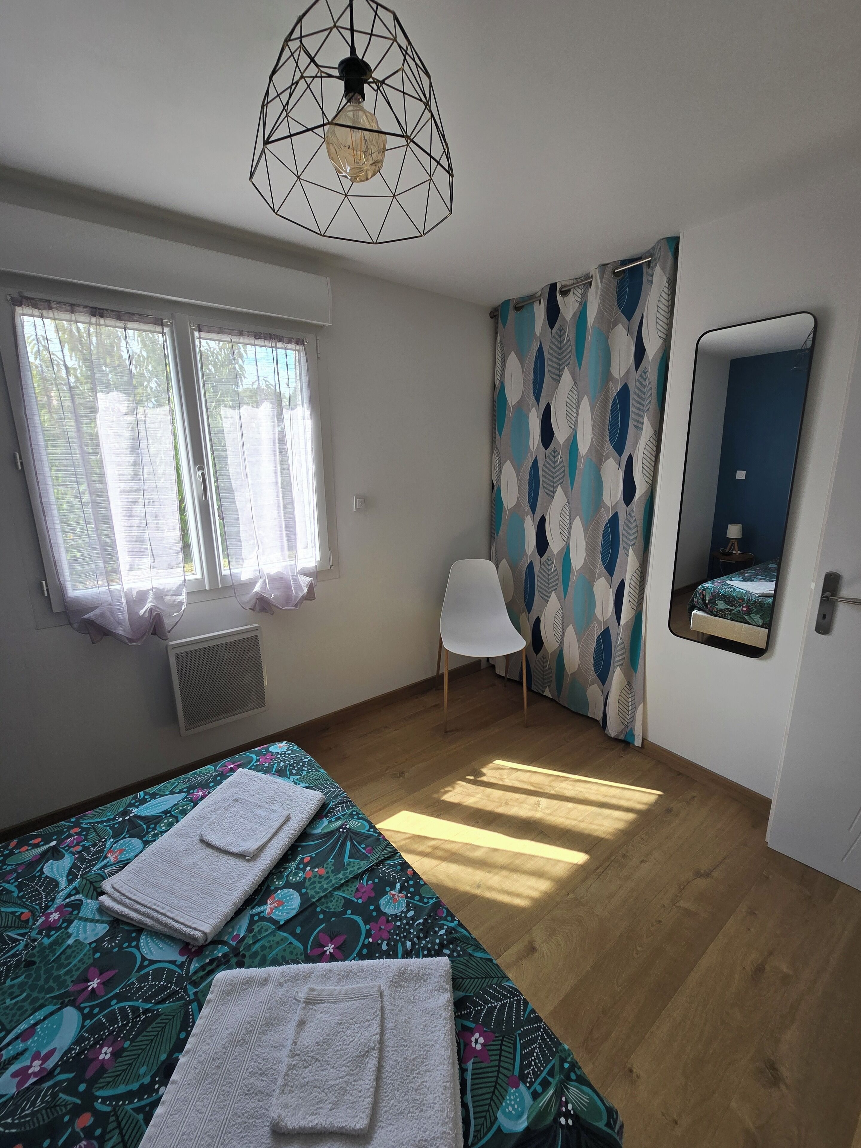 Une chambre à coucher avec un lit, une chaise, une fenêtre et un miroir.