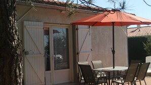 Een terras buiten met een tafel en stoelen, een rode parasol en een schuifdeur.