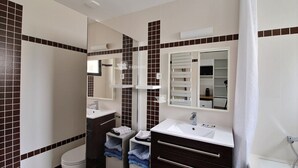 Un baño con un lavamanos blanco, baldosas marrón oscuro, un espejo y una cortina de ducha.