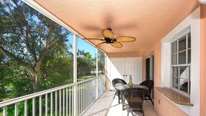Un balcon abrité, doté d'un ventilateur de plafond, de meubles en osier et offrant une vue sur des arbres et un immeuble.