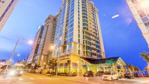 A high-rise hotel with multiple floors, a prominent entrance, and a well-lit facade. - Luxury Beachfront Resort 1BR Suite w/ Full Kitchen in VA Beach Sleeps 4+ (Virginia Beach)