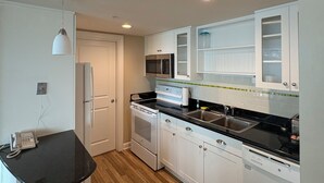 A compact kitchen with white cabinetry, a black countertop, a built-in microwave, a stove, and a refrigerator. - Luxury Beachfront Resort 1BR Suite w/ Full Kitchen in VA Beach Sleeps 4+ (Virginia Beach)