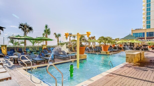 A pool area with lounge chairs, umbrellas, and a water feature. - Luxury Beachfront Resort 1BR Suite w/ Full Kitchen in VA Beach Sleeps 4+ (Virginia Beach)