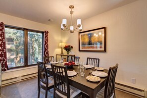Uma sala de jantar com uma mesa redonda posta para seis pessoas, rodeada por cadeiras de madeira.