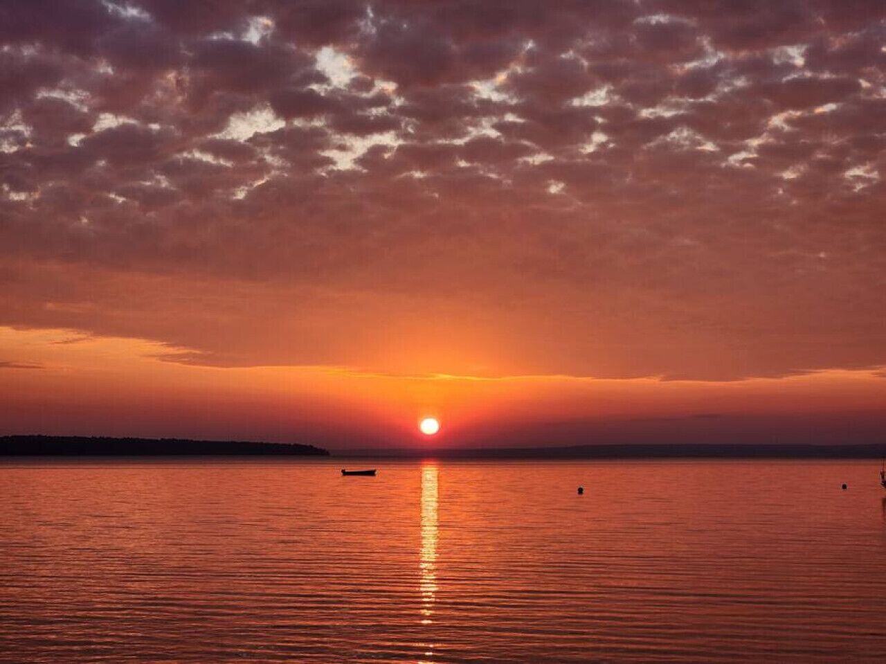A sunset over a calm body of water with a boat in the foreground.