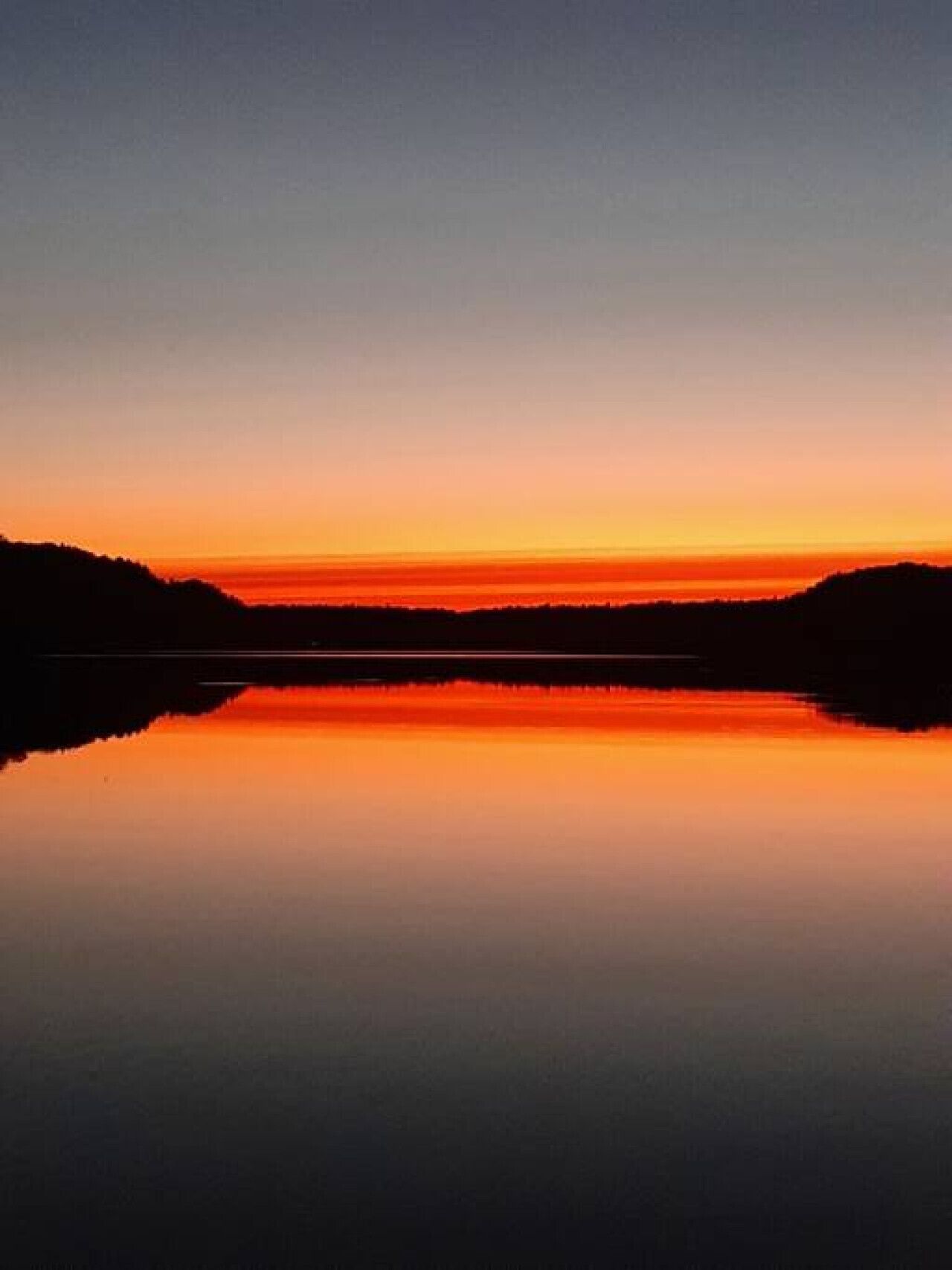 Un llac tranquil que reflecteix un capvespre sota un cel serè.