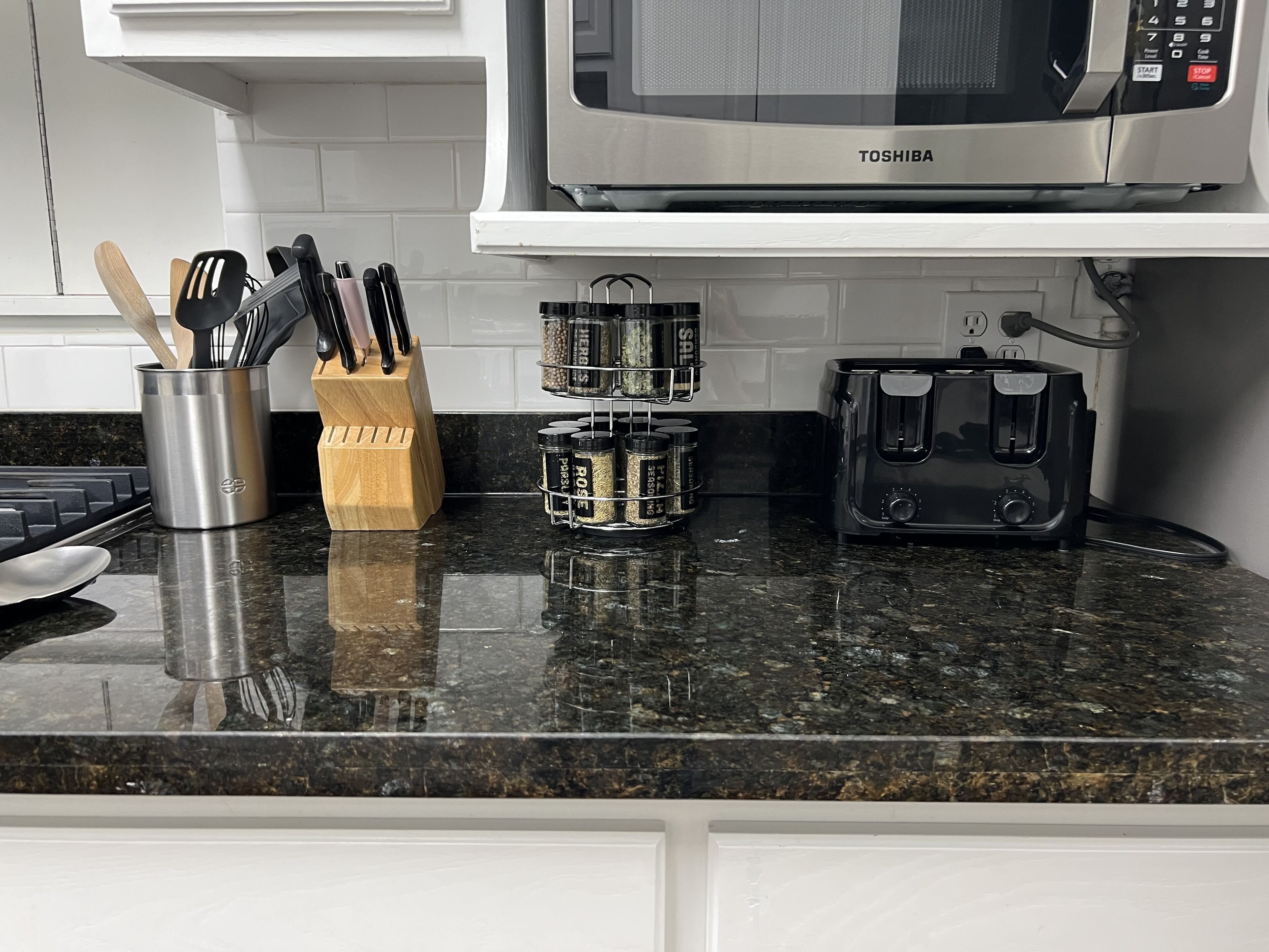 A kitchen counter with a microwave, spice rack, knife block, and toaster.
