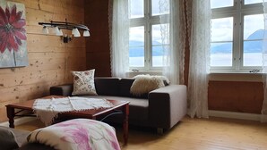 A cozy living room with a wooden wall, a sofa, a coffee table, and a painting. - Irenegarden (Volda)