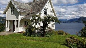 A white house with a sloped roof, a chimney, and a large window. - Irenegarden (Volda)
