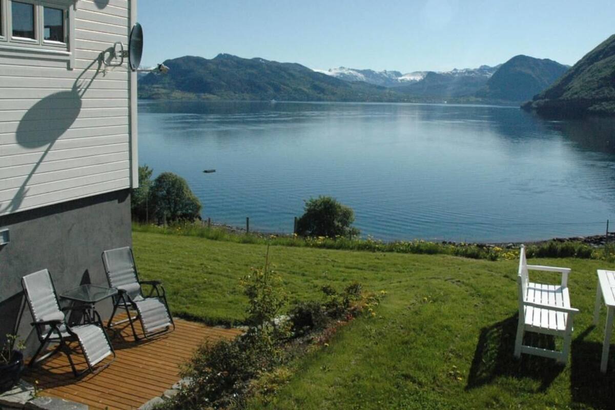 A house with a deck overlooking a calm lake and mountains.