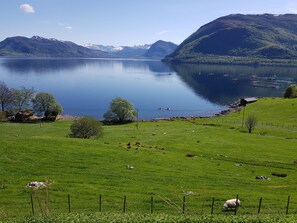 A serene lakeside view with a grassy foreground, a small building, and mountains in the background. - Irenegarden (Volda)