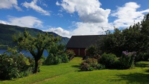 A house with a dark roof, surrounded by lush greenery and a lake. - Irenegarden (Volda)