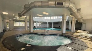 A large indoor pool area with a hot tub, surrounded by stone flooring and a covered seating area.