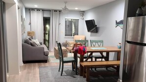 A modern kitchen with a dining area, wooden flooring, and a grey sofa.