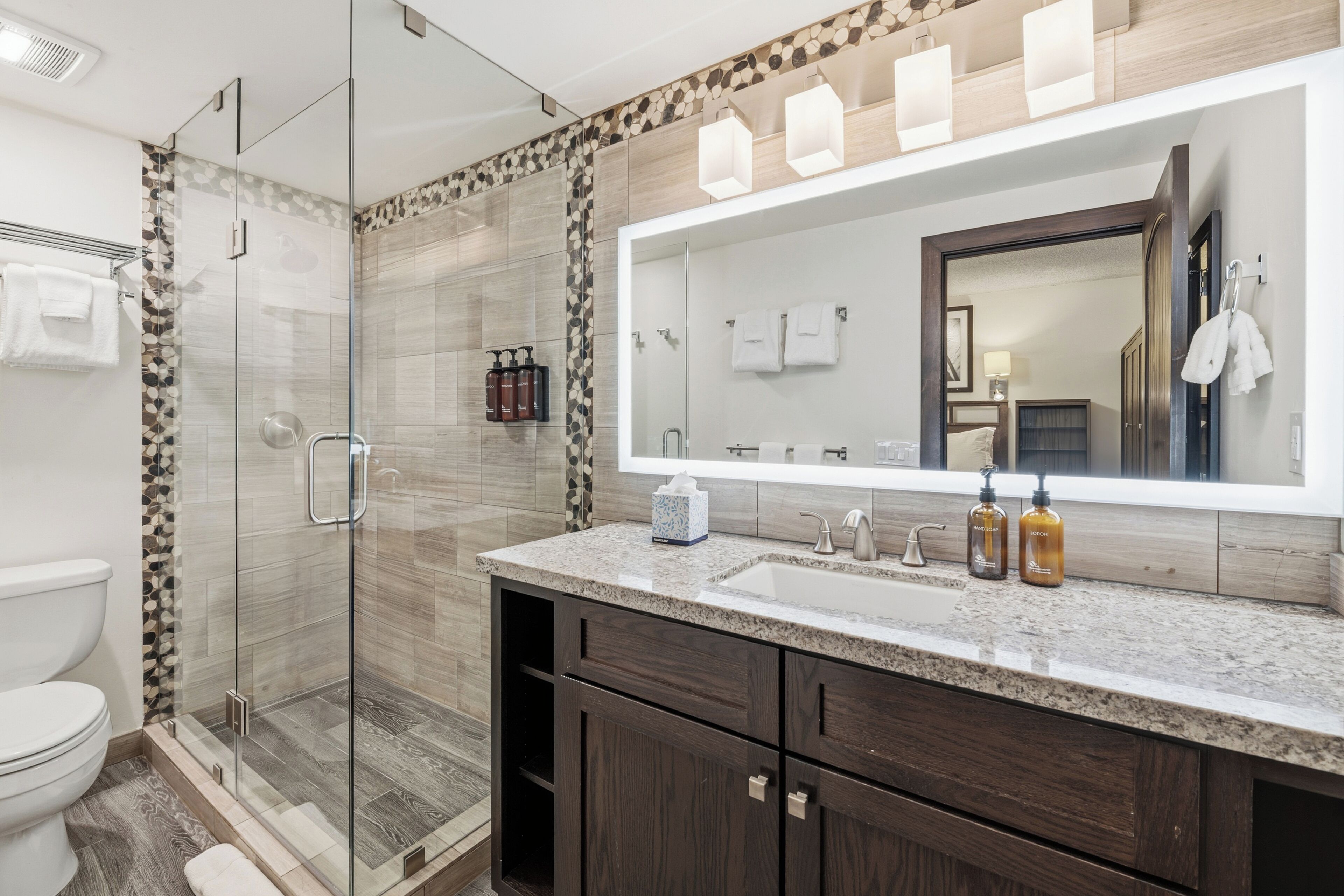 A modern bathroom with a glass shower enclosure, a large mirror, and dark wooden cabinets.