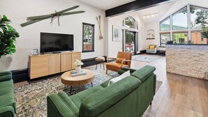 A modern living room with a large TV, green sofas, a wooden cabinet, and a stone accent wall.