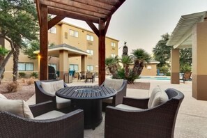 An outdoor seating area with wicker furniture, a round table, and a pool in the background.