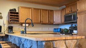 Una cocina con armarios de madera, una isla de piedra, taburetes de bar, un microondas y una cafetera.