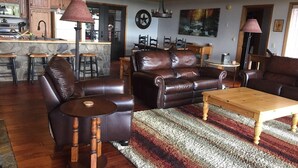 Amplia sala de estar con sofás de cuero, una mesa de centro de madera y una cocina con encimera de piedra y taburetes de bar.